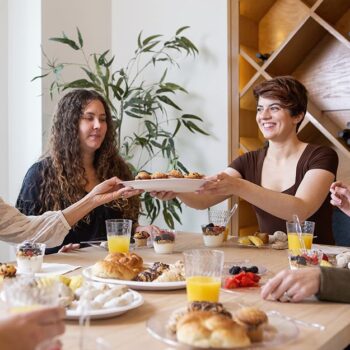 Women passing a Chinet Classic plate with muffins on it