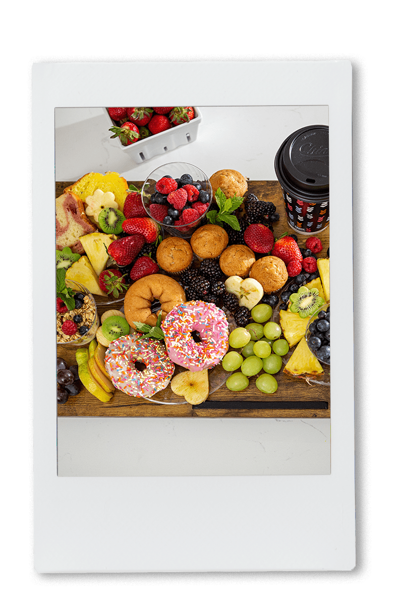 Instax picture of an assortment of fruit and donuts on a cutting board