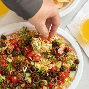 Hand dipping tortilla chip into 7 layer dip on a Chinet Classic platter