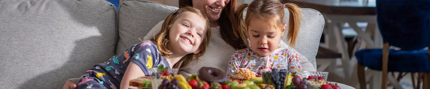 Mom and two daughters sitting on a couch with a tray of fruit