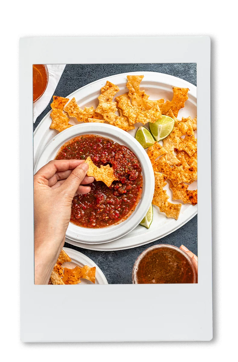 A hand dipping a bat-shaped chip in salsa served in Chinet Classic products