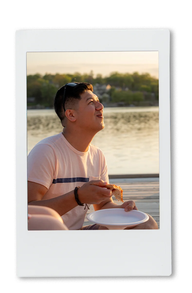 guy laughing and eating pizza on a chinet plate at the lake