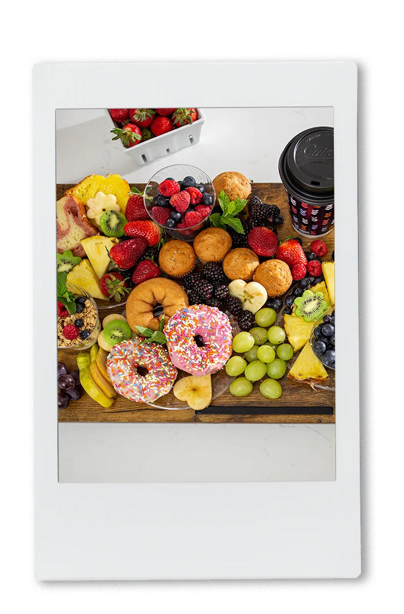 Instax picture of an assortment of fruit and donuts on a cutting board