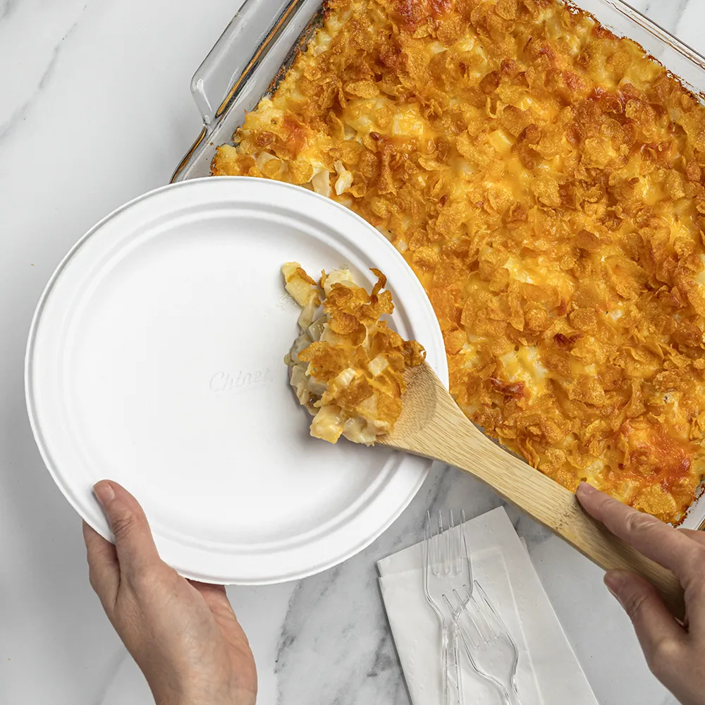 Person dishing out cheesy potato bake onto a chinet plate